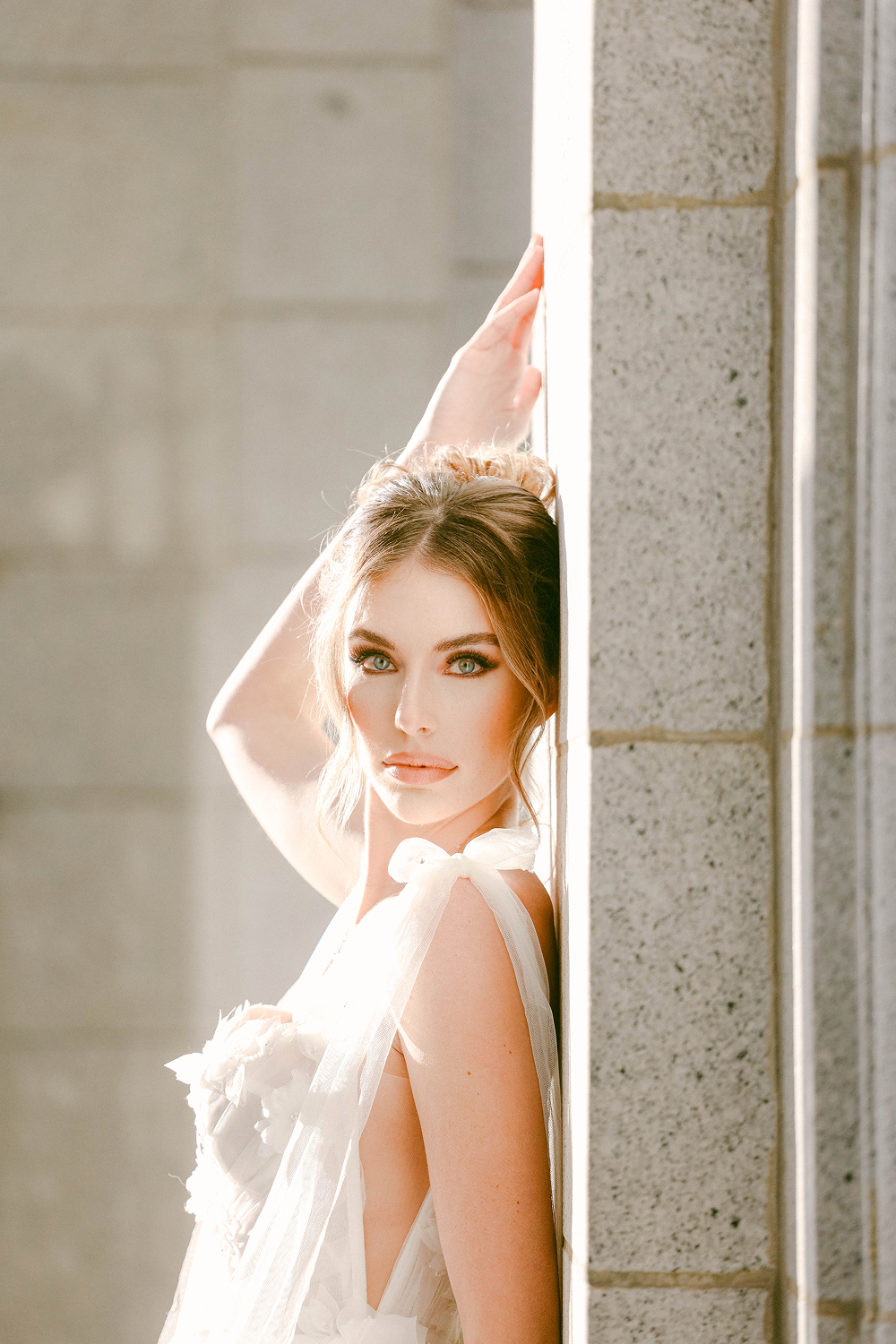Bride in sunlight leaning against concrete wal